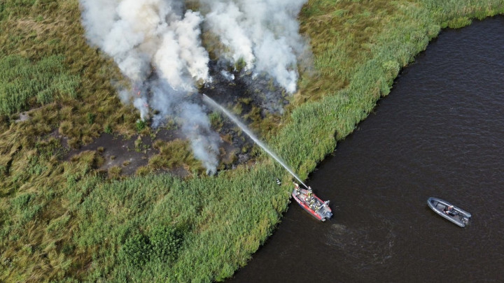 Vanuit de blusboot wordt de brand in de rietkraag geblust. (Dronefoto: Klaas-Jan de Haan)