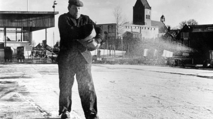 Werknemer Hondema strooit zout op het winterse werfterrein van Halbertsma. Foto uit de jaren ‘60.