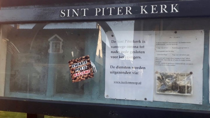 De sticker ‘Zwarte Piet is racisme’ op het glas van het mededelingenkastje bij de kerk.